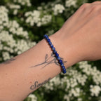Pulsera lapislázuli en la muñeca, elaborada con piedras azules y motas doradas, destacando su belleza natural.
