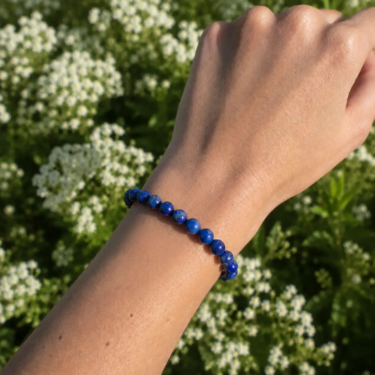Pulsera lapislázuli en la muñeca, elaborada con piedras azules y motas doradas, destacando su belleza natural.